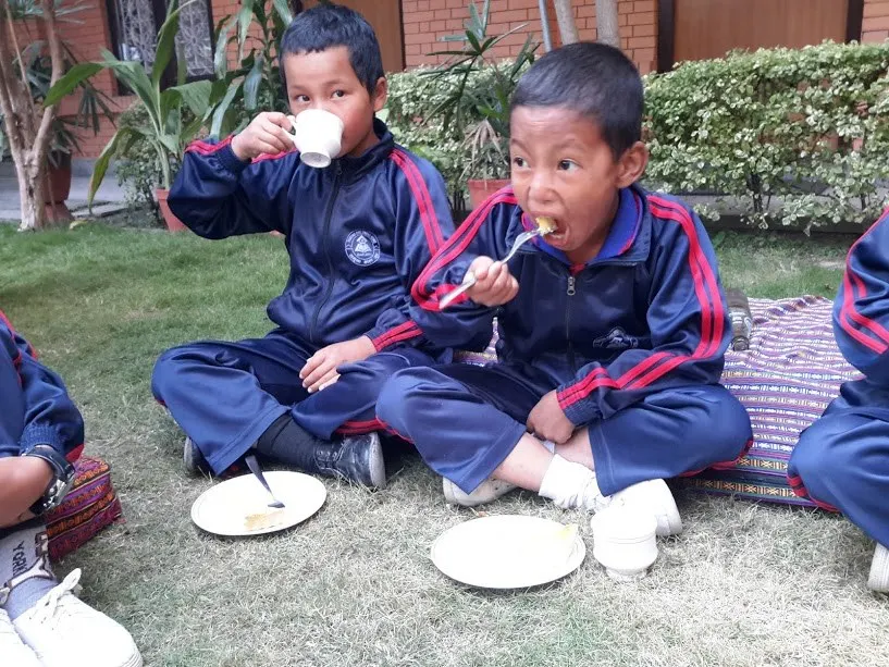 Two children eating a meal from plates while sitting on the grass