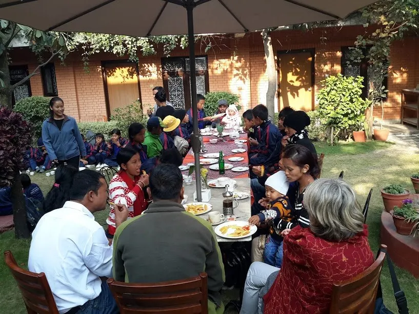 Children and adults seated at tables in a garden for a celebration meal