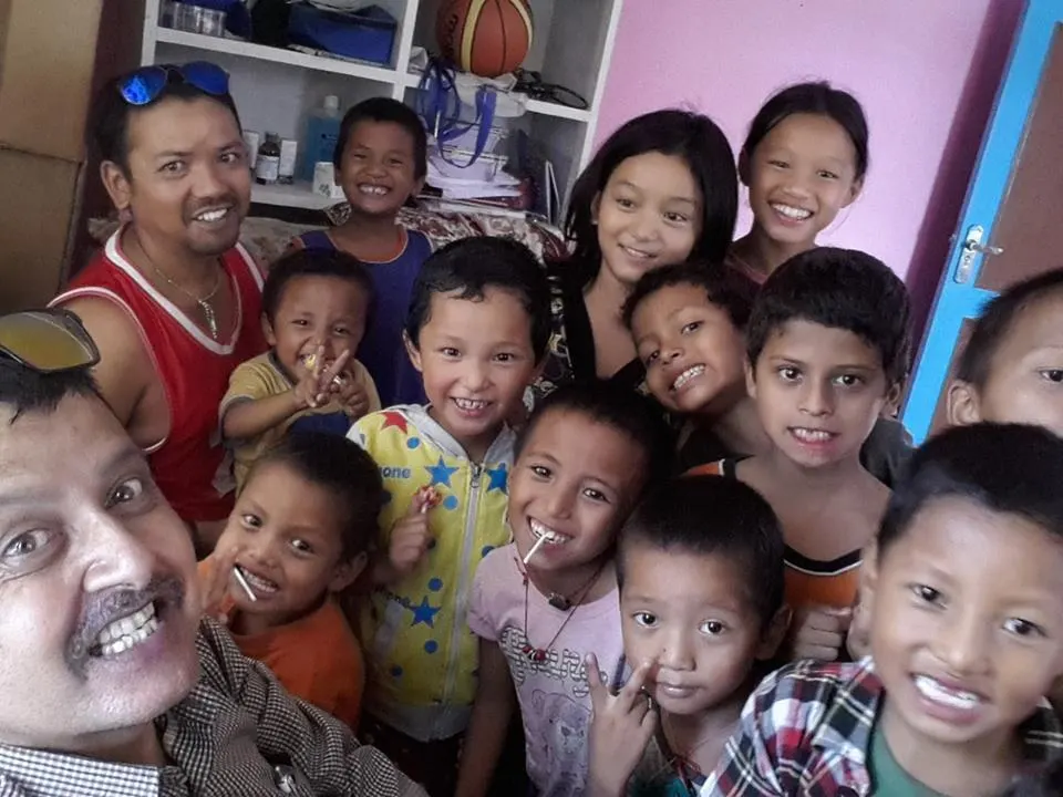 A crowd of children laughing together around two adults
