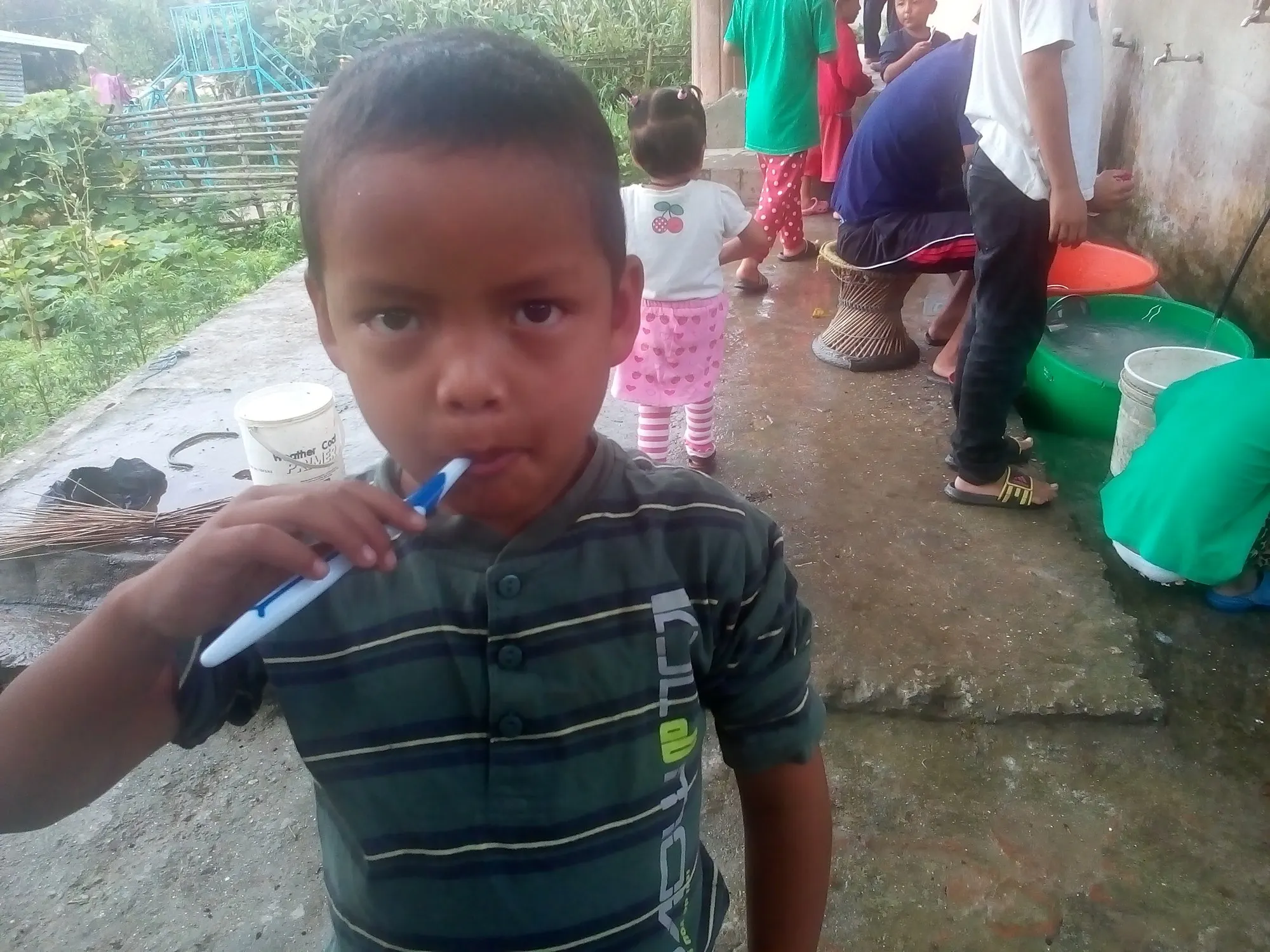 A child brushing teeth while others wash up behind him