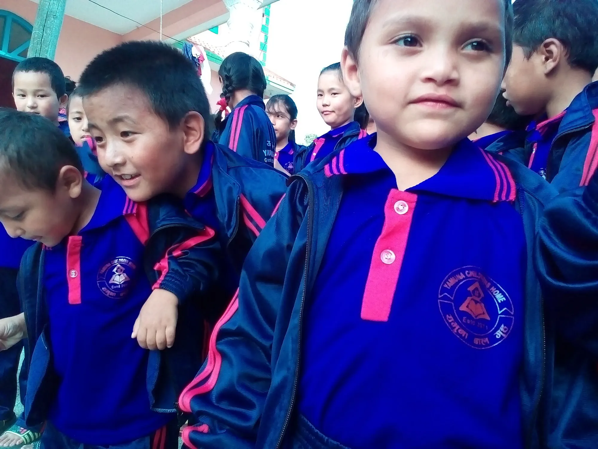 A young child in a blue school tracksuit smiling at the camera