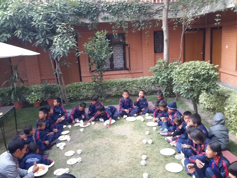 Children sitting in a wide circle on the lawn sharing a meal